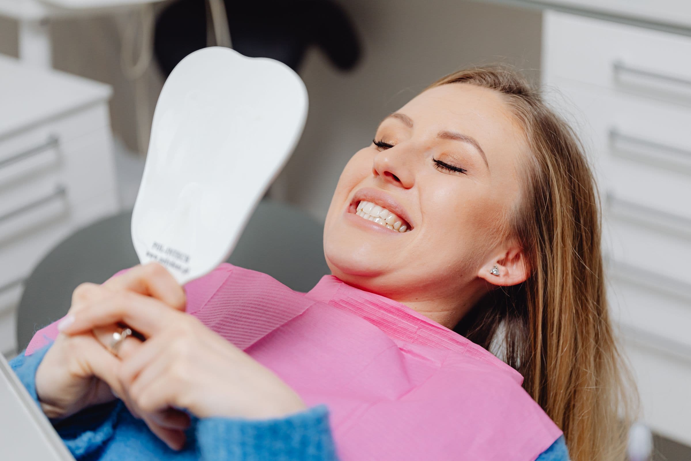 Smiling patient admiring her healthy smile in a hand mirror after a dental visit
