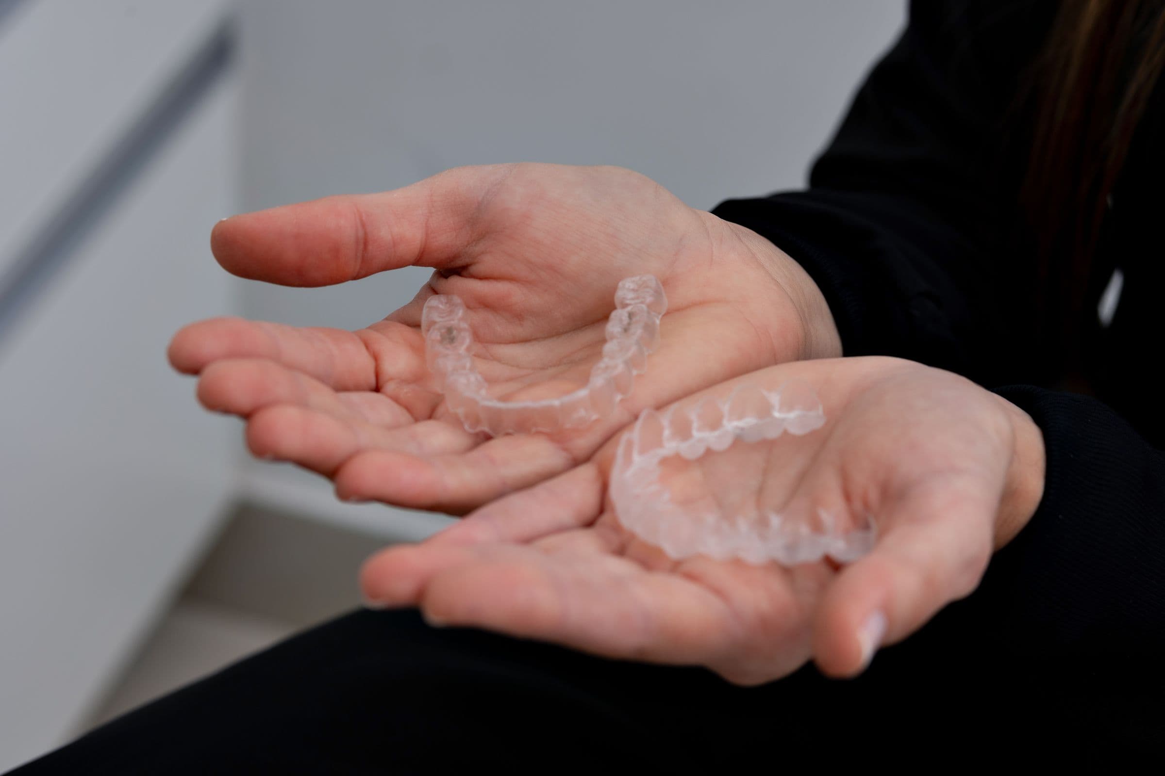 Hands holding upper and lower clear aligner trays in a dental office